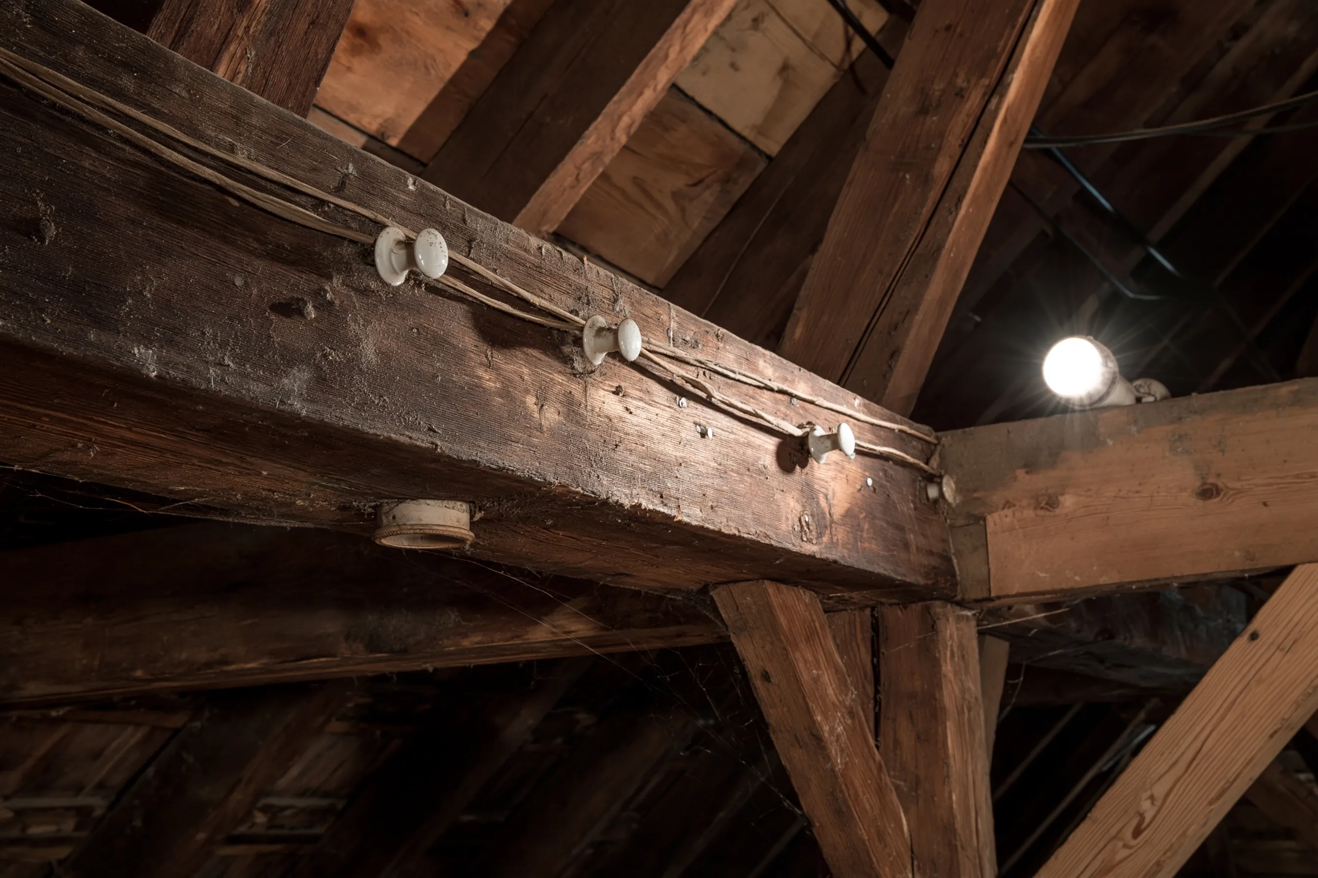 Old attic beam with original knob-and-tube wiring: cloth-covered wires held on white porcelain knobs along the timber